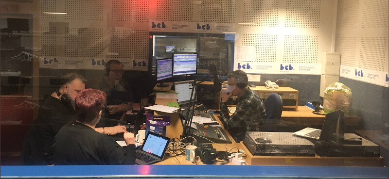 A photo of a group of people sitting around the radio recording desk
