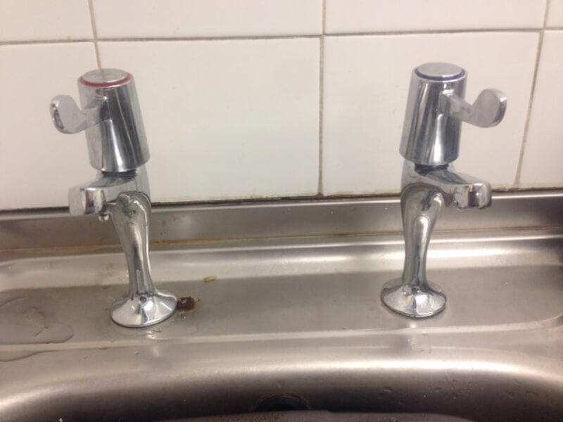 Two silver taps, one with a red band and the other blue, infront of white kitchen tiles
