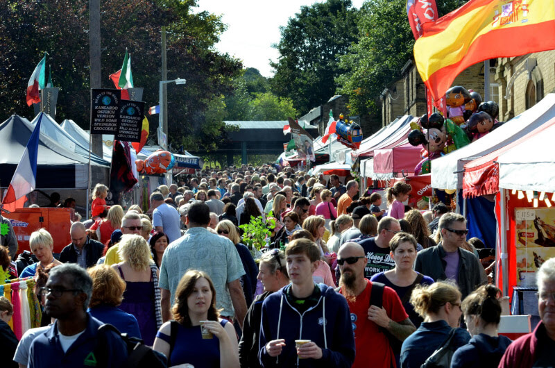a large moving crowd of people walking down a road with marquees and tents on either side