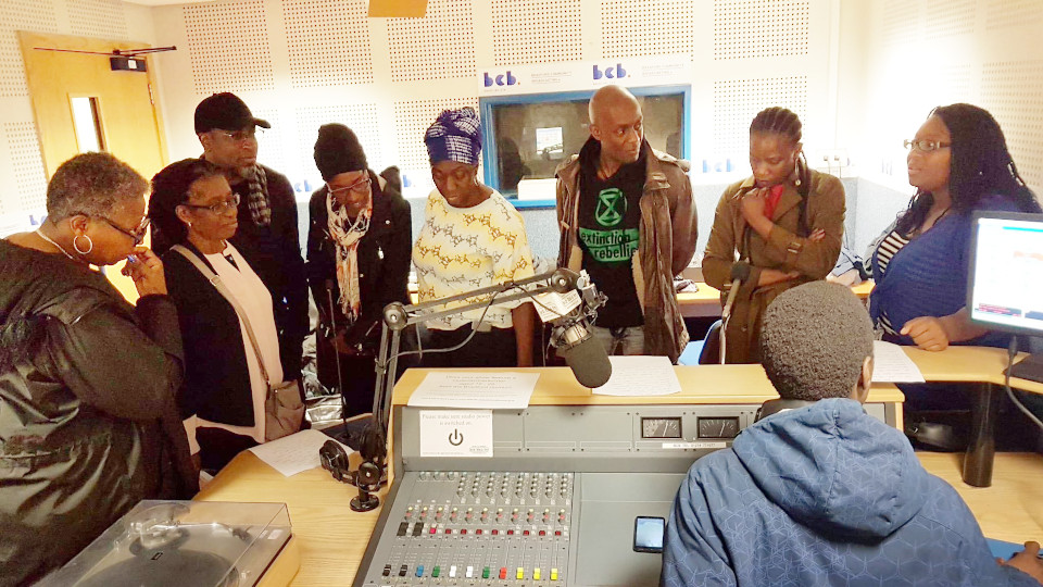 A diverse group of people looking pensive around the radio recording desk